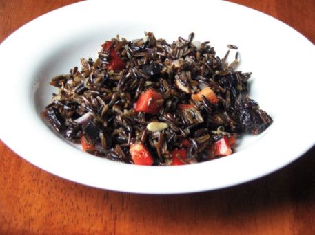 A plate of wild rice with diced vegetables on a wooden table.