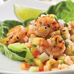 Grilled shrimp served on a bed of lettuce with diced tropical fruits and a lime wedge.