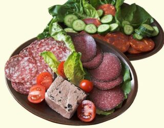 Two mahogany-colored plates containing paleo diet-approved food like tomatoes, lettuce, cucumbers, and meat slices